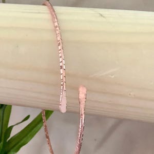 Könnte beinhalten: Ein roségoldenes Armkettchen mit einem strukturierten Design. Das Armband ist offen und hat einen schlichten, eleganten Look.