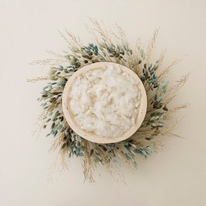 May include: A white bowl filled with white fluffy material, surrounded by a wreath of dried grasses and blue flowers.