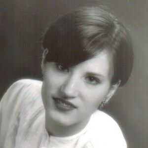 May include: Black and white portrait of a woman with short, straight hair. She is wearing a white blouse and has a neutral expression.