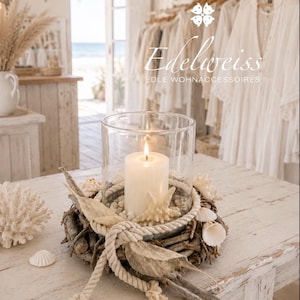 Könnte beinhalten: Ein zylindrischer Glaskerzenhalter mit einer weißen Stumpenkerze, umgeben von einer dekorativen Basis aus Treibholz, weißem Seil, Muscheln und einem Seestern. Der Text Edelweiss EDLE WOHNACCESSOIRES ist im oberen Bildbereich zu sehen.