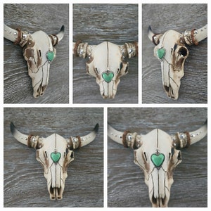 May include: Five white ceramic bull skulls with turquoise heart-shaped accents. Each skull has rhinestones and a beaded rope detail on the horns.
