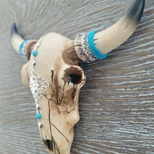 May include: A white ceramic bull skull with turquoise and silver accents. The skull is decorated with a silver filigree design and turquoise beads. The horns are black and white.