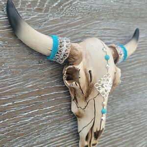May include: White ceramic bull skull with turquoise and silver accents. The skull has a distressed finish and is decorated with turquoise beads and silver filigree.