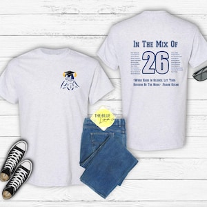 May include: Light gray t-shirts with a graduation theme. One shirt has a small graphic of a graduate and the other has the text "IN THE MIX OF 26" with a quote. The image also includes blue jeans, black sneakers, and sunglasses.
