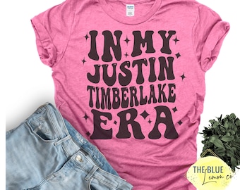 May include: A pink t-shirt with the text "IN MY JUSTIN TIMBERLAKE ERA" in a retro font. The shirt is paired with light blue denim shorts. The Blue Lemon Co. logo is visible in the bottom right corner.