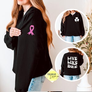 May include: Black sweatshirt with a pink ribbon on the sleeve. Additional images show a sweatshirt with a white shamrock and another with the text "LIVE LIKE DEE" in white. The Blue Lemon Co. logo is visible.