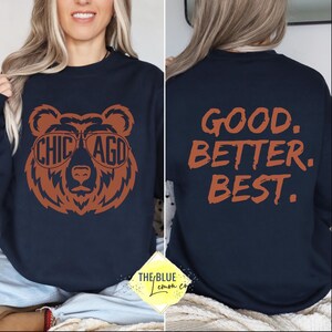 May include: Navy blue sweatshirt featuring a brown bear graphic wearing sunglasses with "CHICAGO" and "AGD" on the lenses. The back of the sweatshirt displays the text "GOOD. BETTER. BEST." in orange. The Blue Lemon Co. logo is at the bottom.