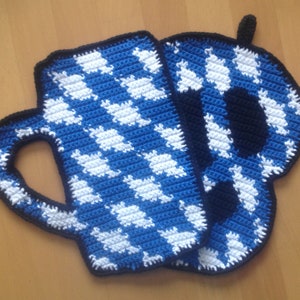 Könnte beinhalten: Gehäkeltes Topflappen- und Untersetzer-Set in Becherform. Das Set hat ein blau-weißes Karomuster mit schwarzem Rand. Der Topflappen in Becherform hat einen Henkel. Der Untersetzer hat eine passende Form.
