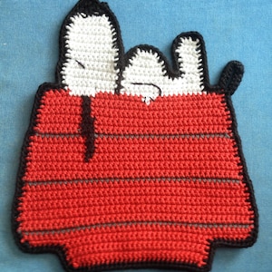 Könnte beinhalten: Häkel-Hundehütte mit zwei weißen Hunden, die aus der Oberseite schauen. Das Haus ist rot mit schwarzem Besatz und grauen Streifen.