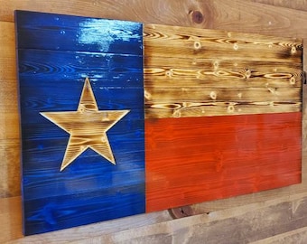 May include: A wooden Texas flag with a blue and red background and a white star. The flag is made of reclaimed wood and has a rustic, distressed look.