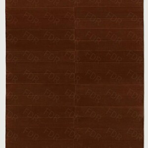 May include: A rectangular brown rug with a repeating pattern of the letters "FDR" in a lighter shade of brown. The rug is divided into horizontal rectangular sections.