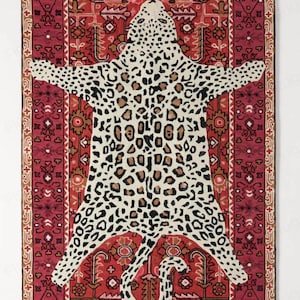 May include: A rectangular rug with a leopard skin design in the center, surrounded by a red and brown patterned border. The leopard print features black and brown spots on a cream background. The rug has a decorative, tribal-inspired design.