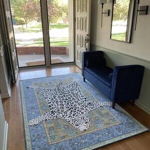 May include: A blue area rug with a detailed border and a leopard print rug on top. The leopard print rug is white with black spots. The room has a blue bench, a mirror, and a door.