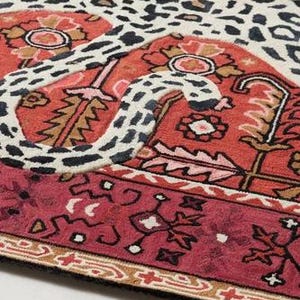 May include: A patterned rug with a leopard print design in cream, brown, and black, combined with a red and burgundy border featuring floral and geometric patterns. The rug has a black edge.
