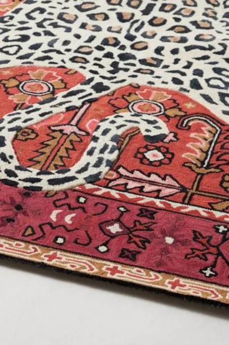 May include: A patterned rug with a leopard print design in cream, brown, and black, combined with a red and burgundy border featuring floral and geometric patterns. The rug has a black edge.