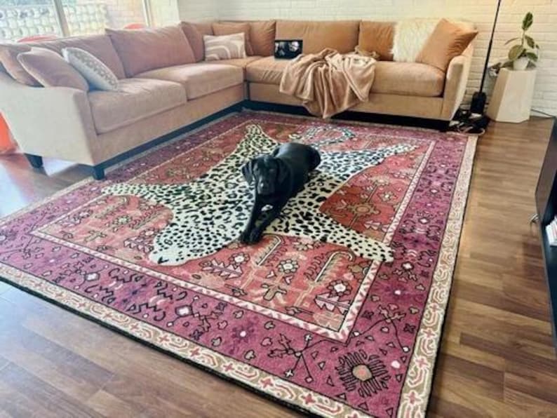 May include: A large, rectangular area rug with a detailed, patterned border in shades of burgundy, beige, and black. The rug features a central leopard print design, and a black dog is lying on top of the rug.