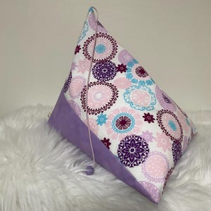 Pode incluir: Uma almofada de cunha roxa e branca com um tassel. A almofada é feita de tecido com um design de mandala.