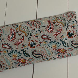 Può includere: Pochette rettangolare in tessuto con motivo paisley rosso, turchese e oro su sfondo grigio chiaro. La pochette ha una piccola etichetta bianca con la parola "von" e un simbolo a forma di cuore.