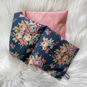 Peut inclure: Une bouillotte en tissu floral bleu foncé avec une housse en tissu rose. La bouillotte a une étiquette blanche avec le mot "fait main" dessus.