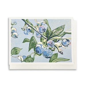 May include: A rectangular greeting card featuring a block print illustration of blueberries on a branch with green leaves against a light blue background. The artwork displays a textured, layered ink effect with shades of blue, green, and white.