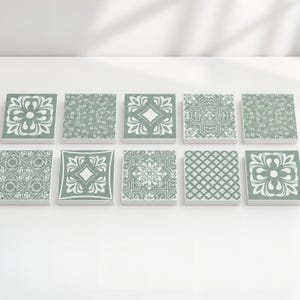 May include: A collection of ten square tiles arranged in two rows of five. Each tile features a sage green background with white printed patterns, including floral motifs, geometric shapes, intricate scrollwork, and repeating diamond designs.
