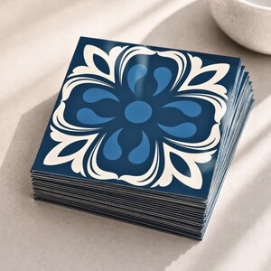 May include: A stack of square tiles featuring a dark blue background with a symmetrical floral pattern in lighter blue and cream white. The tiles have a smooth, glossy finish and are arranged in a neat, aligned pile with visible edges.