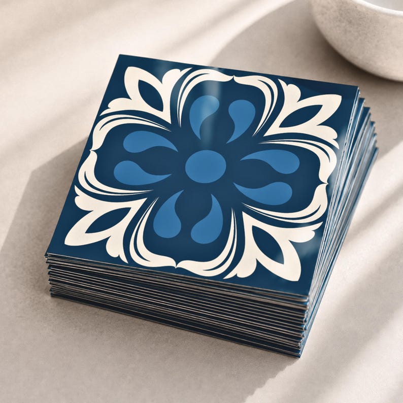 May include: A stack of square tiles featuring a dark blue background with a symmetrical floral pattern in lighter blue and cream white. The tiles have a smooth, glossy finish and are arranged in a neat, aligned pile with visible edges.