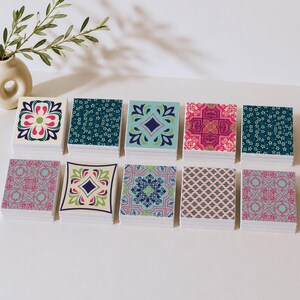 May include: Ten square coasters arranged in two rows, each featuring a distinct colourful pattern. The designs include floral motifs, geometric shapes, and intricate tile-like prints in shades of blue, pink, green, and cream on a white base.