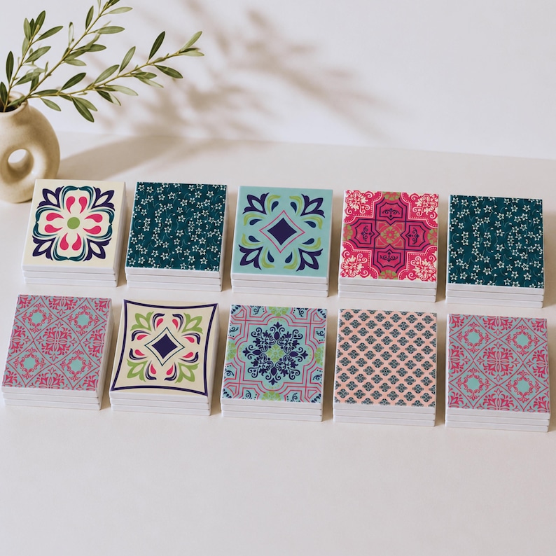 May include: Ten square coasters arranged in two rows, each featuring a distinct colourful pattern. The designs include floral motifs, geometric shapes, and intricate tile-like prints in shades of blue, pink, green, and cream on a white base.