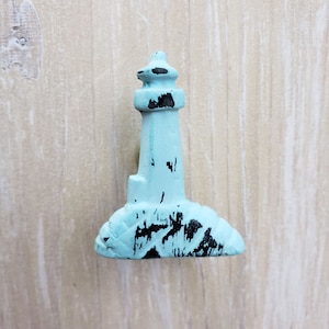 May include: A light blue and black lighthouse-shaped cabinet knob with a distressed finish.