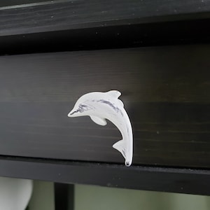 May include: White ceramic dolphin drawer pull. The dolphin is in a jumping pose with a distressed white finish.