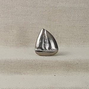 Könnte beinhalten: Eine silberne Segelboot-Figur. Das Segelboot ist detailliert mit einem spitzen Bug und einem einzigen Segel.