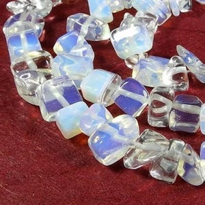 May include: A strand of iridescent white and clear gemstone beads. The beads are faceted and have a slightly irregular shape. The beads are strung on a clear thread.