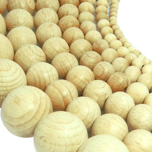 Op de afbeelding: Een close-up van een grote hoeveelheid natuurlijke houten kralen in verschillende maten. De kralen zijn gerangschikt in een halve cirkel, met de grootste kralen in het midden en de kleinste kralen aan de randen. De kralen zijn licht beige van kleur en hebben een gladde, gepolijste afwerking.