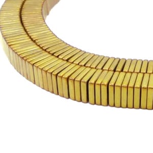 Könnte beinhalten: Eine Strähne aus rechteckigen Perlen in Goldfarbe. Die Perlen sind kreisförmig angeordnet.