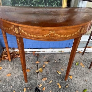 May include: A half-round wooden table with intricate marquetry inlay in a floral pattern. The table has a rich brown finish and delicate legs.