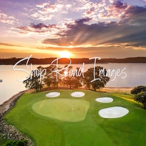May include: Aerial view of a golf course at sunset. The green course is surrounded by sand traps and a lake. The sky is filled with orange, yellow, and purple hues. The text "Shop Road Images" is overlaid on the image.