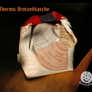 Op de afbeelding: Een witte geïsoleerde lunchtas met een rode band en een bruin-wit geometrisch patroon. De tas heeft een label met de tekst "Greenolog".