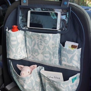 Könnte beinhalten: Ein blauer Autositz-Organizer mit mehreren Taschen. Der Organizer hat eine transparente Plastiktasche für ein Telefon, eine Tasche für eine Wasserflasche und mehrere andere Taschen zum Verstauen von Kleinigkeiten. Der Organizer ist mit einem hellblauen und weißen Fischmuster verziert. Der Text "Kleine Prinz" ist auf einer der Taschen sichtbar.