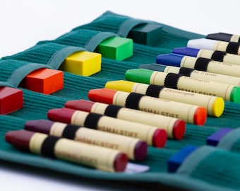 May include: A teal fabric roll-up case with 12 compartments holds a variety of colored crayons and wax blocks. The case has a label that reads "Sigmal Stift" and "Nr. 7 grün".