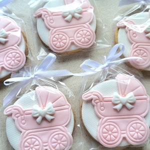 May include: Four pink and white baby carriage cookies decorated with white bows, individually packaged in clear cellophane bags with white ribbons.