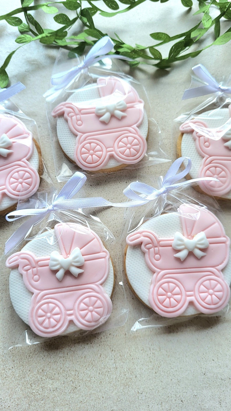 May include: Four pink and white baby carriage cookies decorated with white bows, individually packaged in clear cellophane bags with white ribbons.