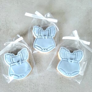 May include: Three blue baby onesie cookies in individual clear cellophane bags tied with white ribbon.