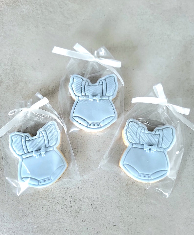 May include: Three blue baby onesie cookies in individual clear cellophane bags tied with white ribbon.