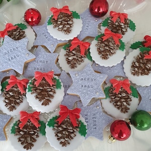 Può includere: Una collezione di biscotti natalizi festivi. I biscotti sono decorati con pigne, fiocchi rossi e foglie di agrifoglio. Alcuni biscotti sono a forma di stella e hanno la scritta "MERRY XMAS". Ornamenti rossi e verdi sono sparsi.