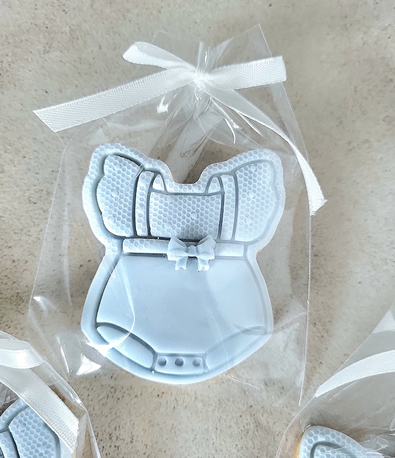 May include: A light blue baby onesie cookie in a clear cellophane bag tied with a white ribbon.