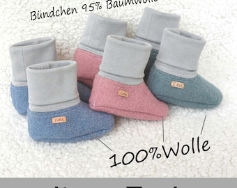 May include: Three pairs of baby booties in blue, pink, and teal. The booties are made of soft, fuzzy fabric and have a gray fold-over cuff. The text "Bündchen 95% Baumwolle" is visible on the top of the image. The text "100% Wolle" is visible in the bottom center of the image. The text "weitere Farben" is visible at the bottom of the image.