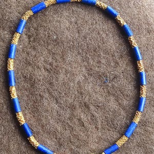 Può includere: Una collana blu e oro con chiusura magnetica. La collana è realizzata con piccole perle rotonde.