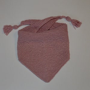 Può includere: Una sciarpa triangolare di maglia rosa con frange su ogni estremità.