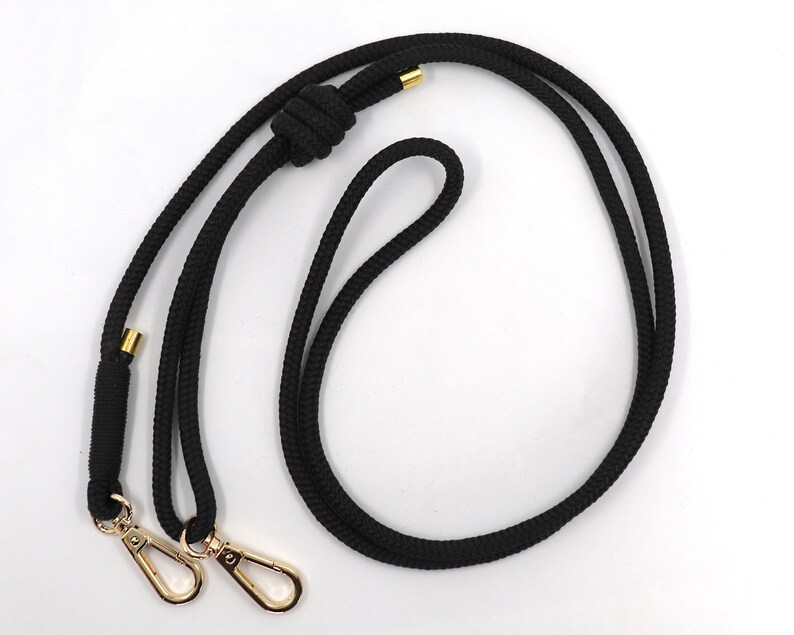 May include: Black rope lanyard with gold-colored metal swivel clasps and accents. The lanyard features a knotted design and is suitable for holding keys, an ID badge, or other small items. The rope is thick and durable.